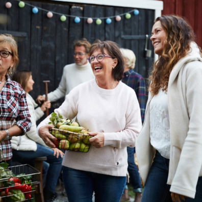 Cheerful women standing with baskets against friends at farm during dinner party